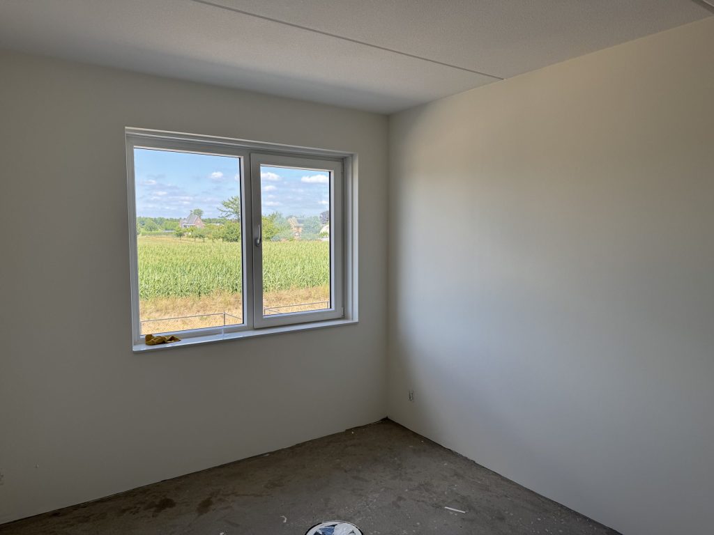 Lege slaapkamer met gladde witte wanden en een raam dat uitkijkt over weiland en bomen