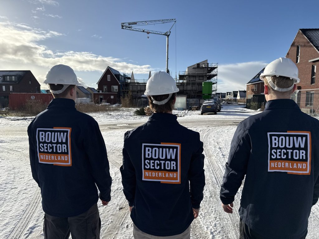 Drie vakmensen van Bouwsector Nederland met witte helm kijken naar een rij nieuwe woningen in aanbouw